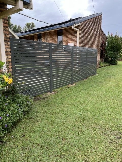 A fence surrounds a lush green yard in front of a brick house — Fabricator In Coffs Harbour, NSW