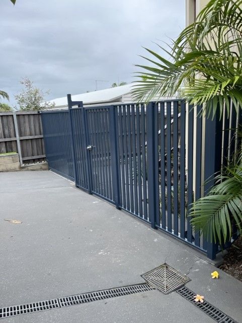 A blue fence is surrounding a driveway next to a palm tree — Fabricator In Coffs Harbour, NSW