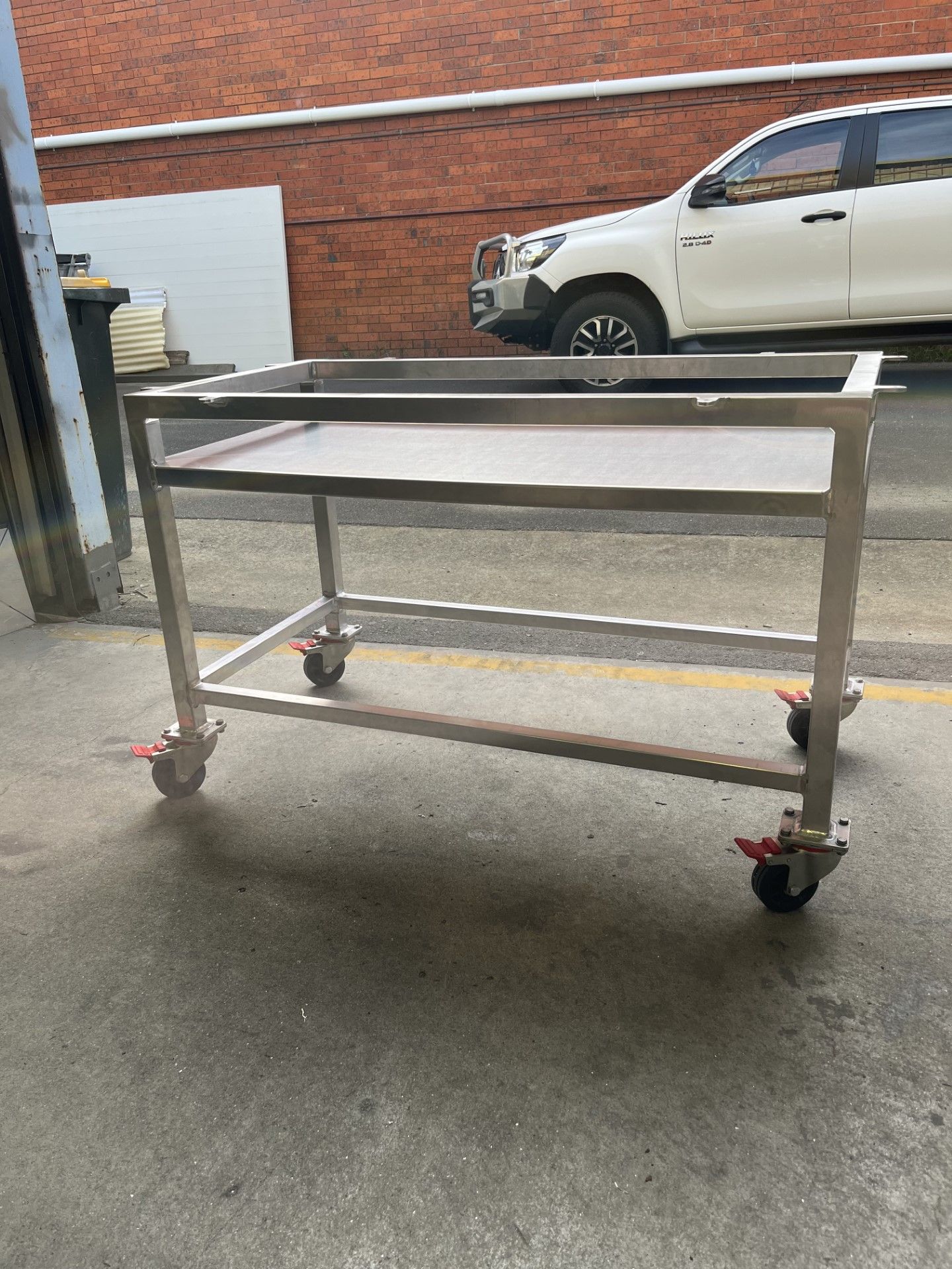 A stainless steel cart with wheels is parked in front of a white car — Fabricator In Coffs Harbour, NSW