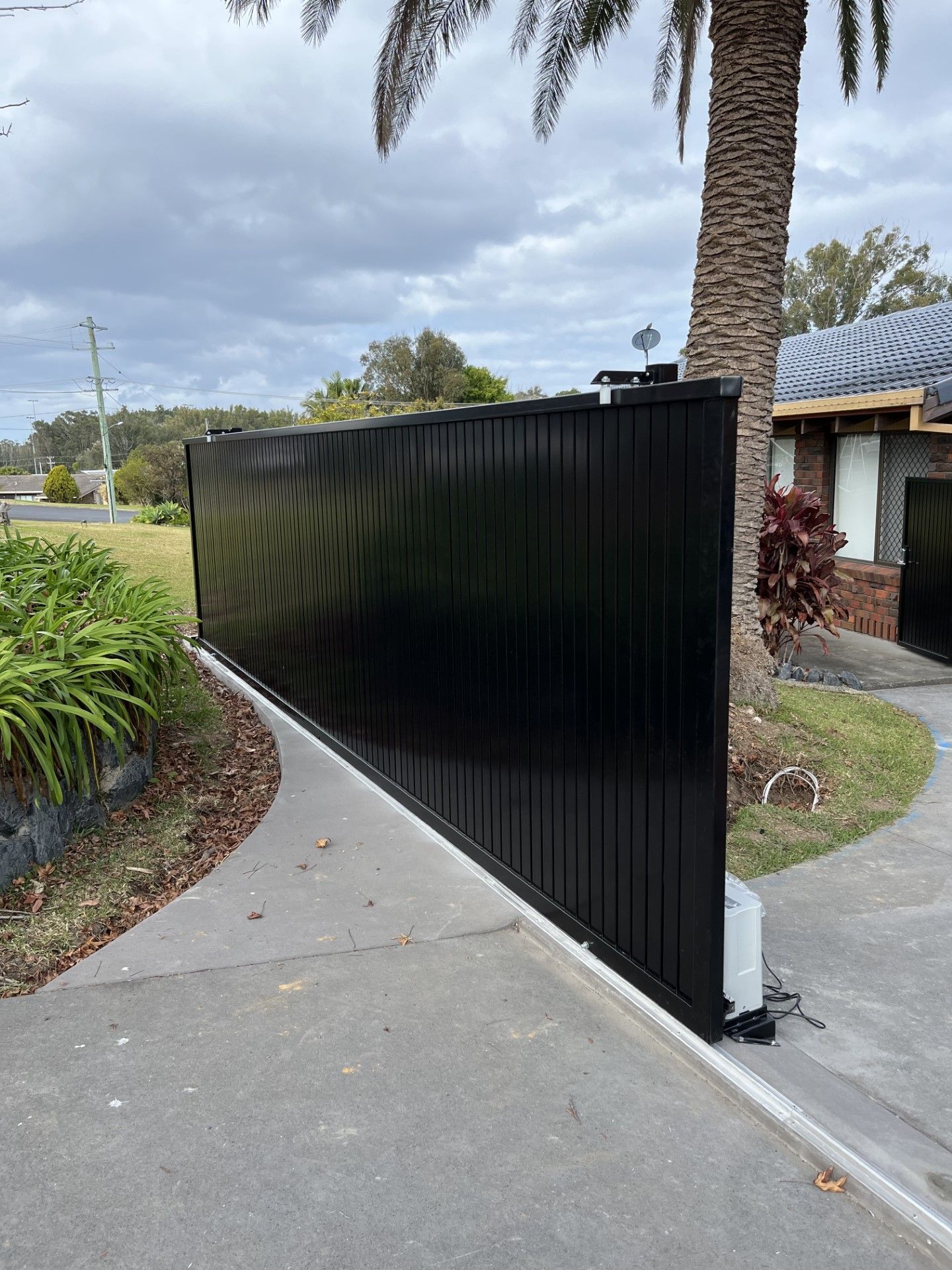 A black fence is sitting next to a palm tree in front of a house — Fabricator In Coffs Harbour, NSW