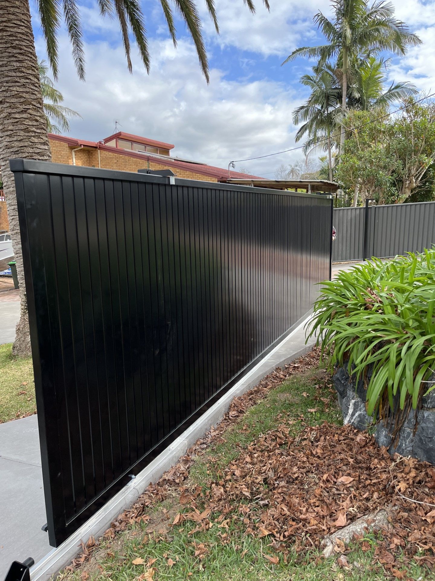 A black fence is sitting on the side of a road next to a palm tree — Fabricator In Coffs Harbour, NSW
