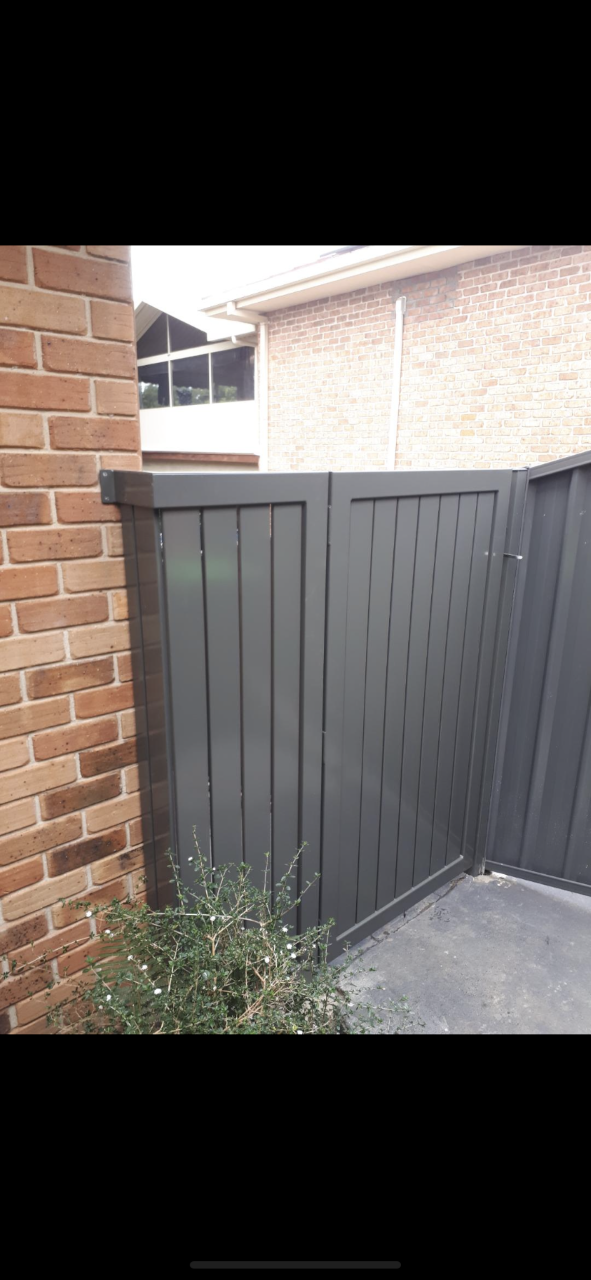A black fence is sitting next to a brick wall — Fabricator In Coffs Harbour, NSW