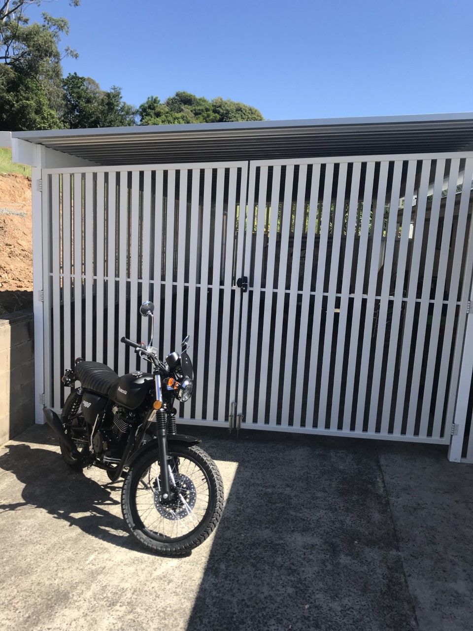 A black motorcycle is parked in front of a white fence — Fabricator In Coffs Harbour, NSW