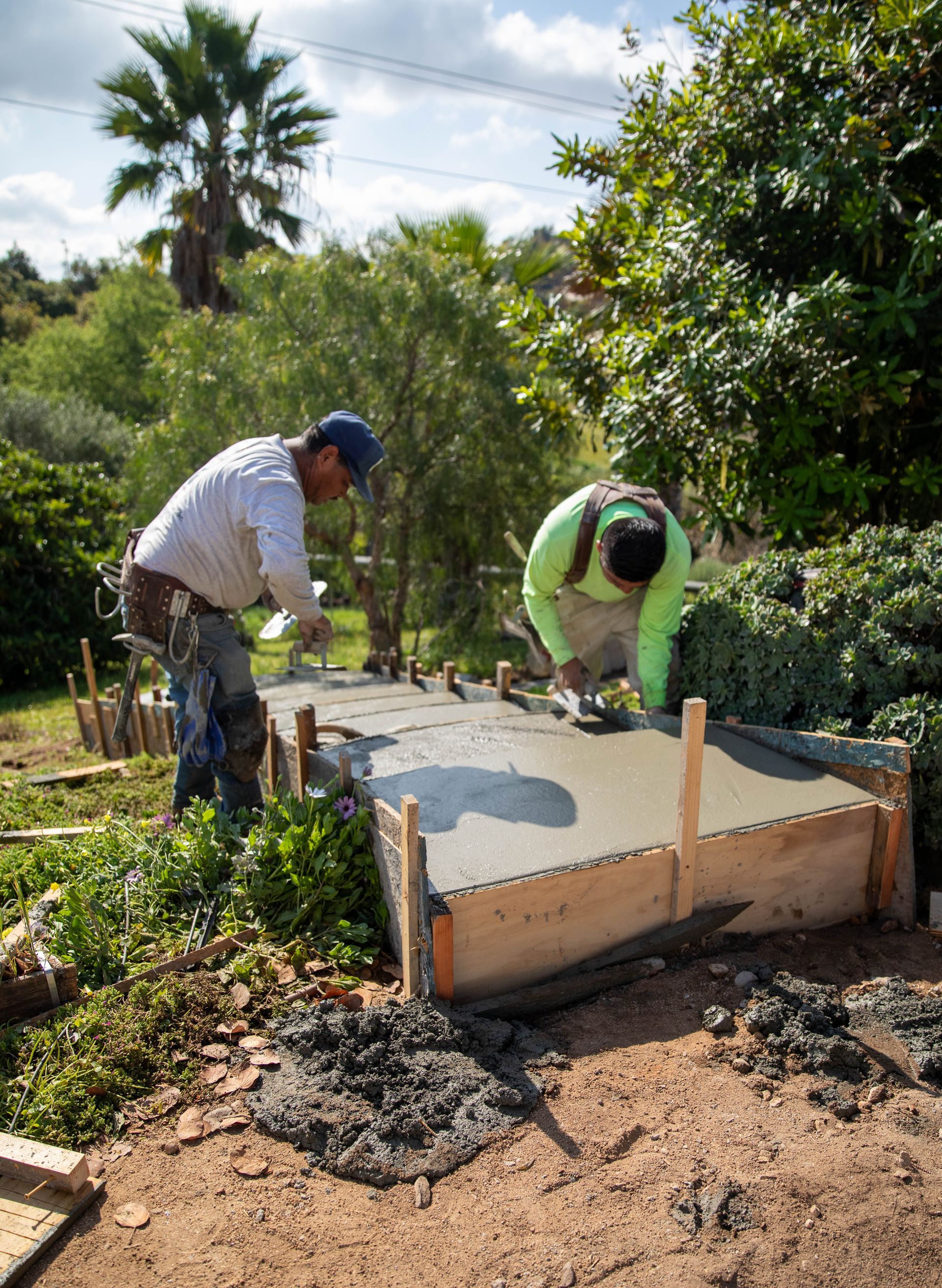 A person operates an orange Kubota mini excavator in a residential backyard with muddy ground.