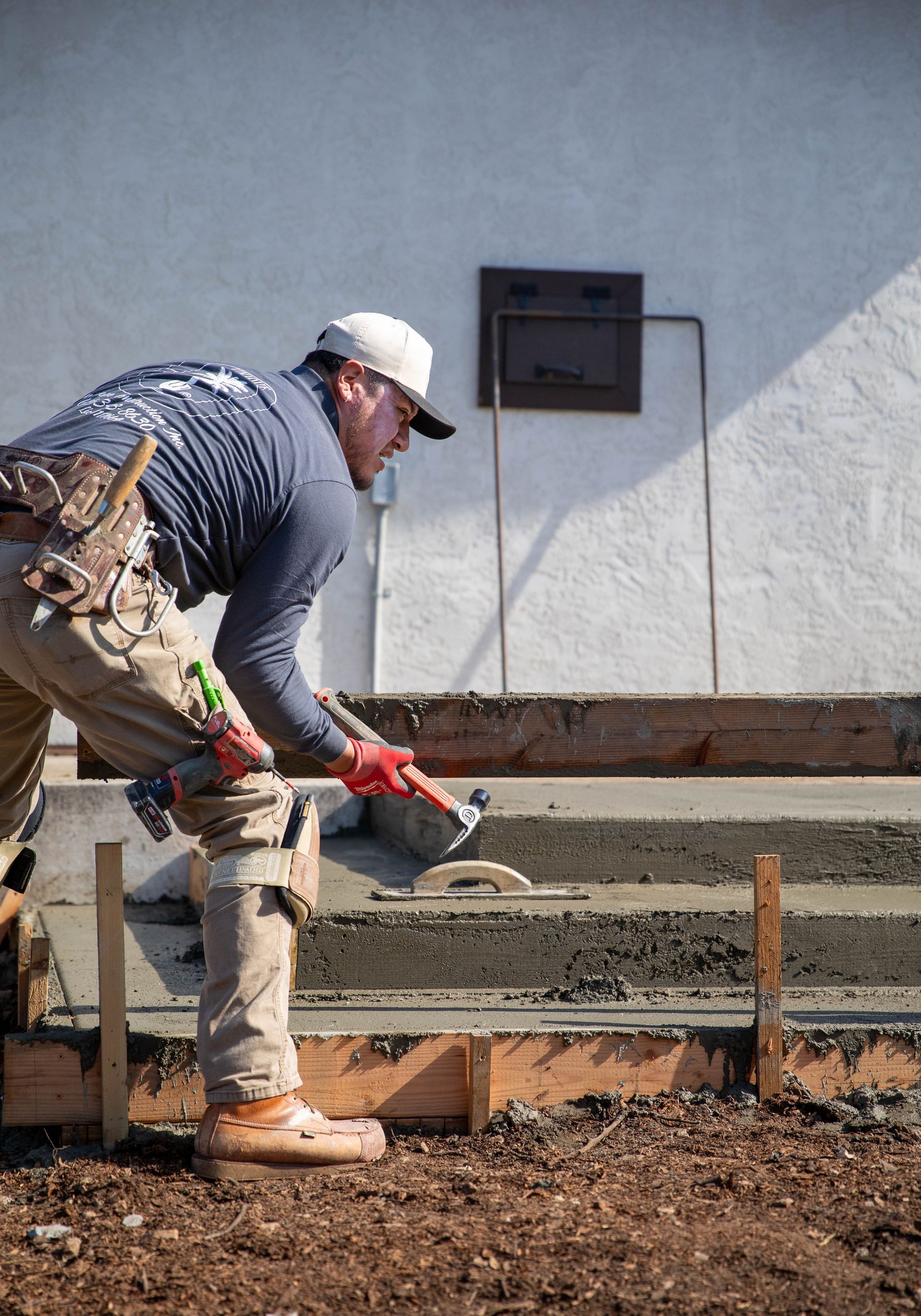 An orange mini excavator parked in a backyard next to two newly constructed concrete retaining walls.