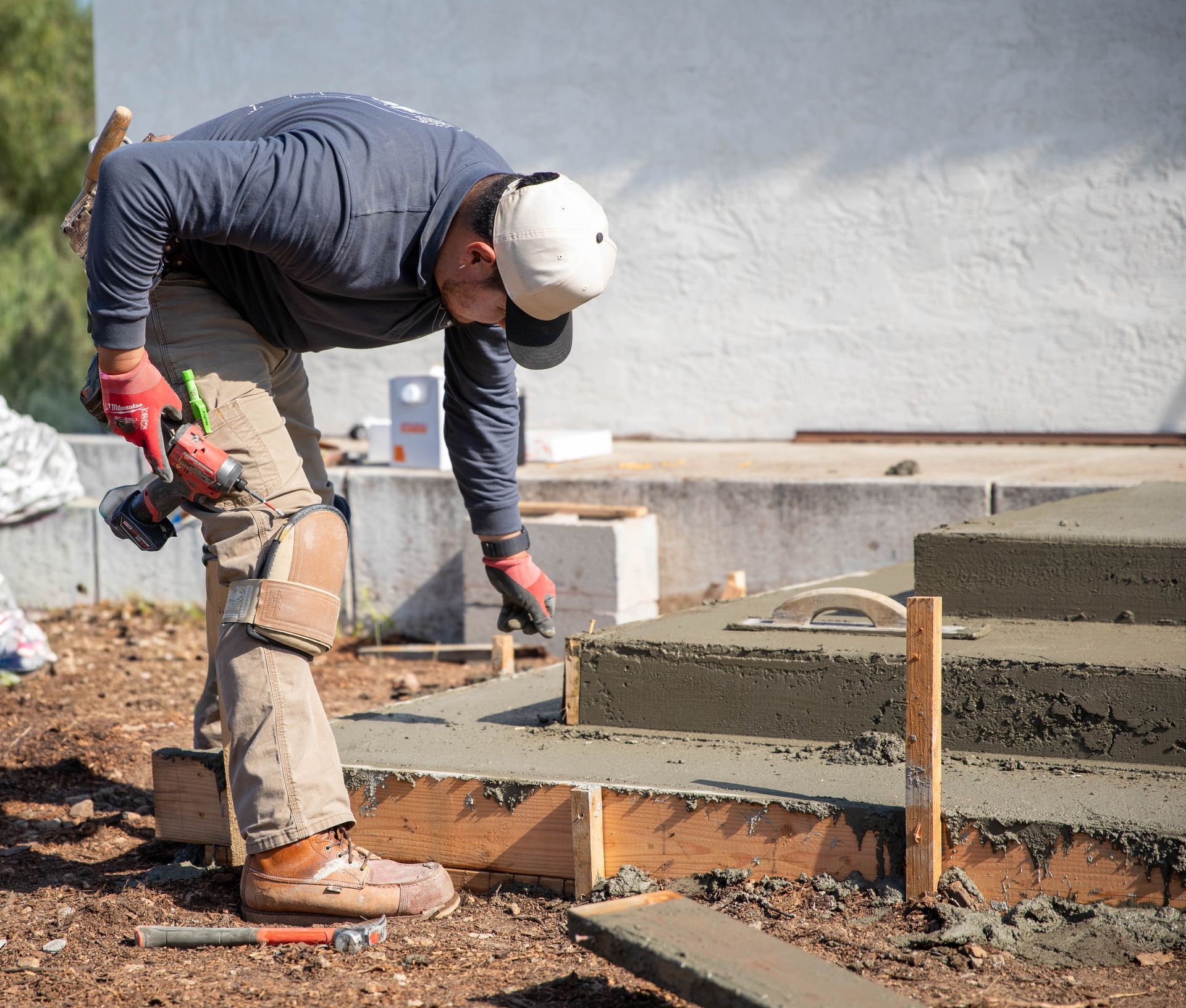 A construction worker uses a tool to smooth wet concrete into wooden forms at a building site.