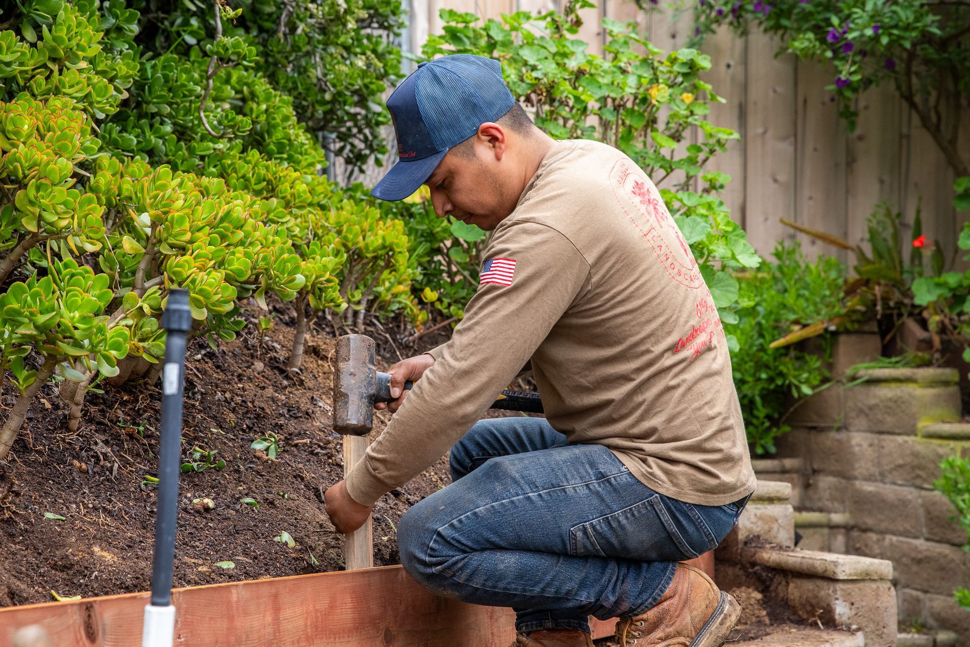 Man in work clothes uses a hammer in a garden bed.