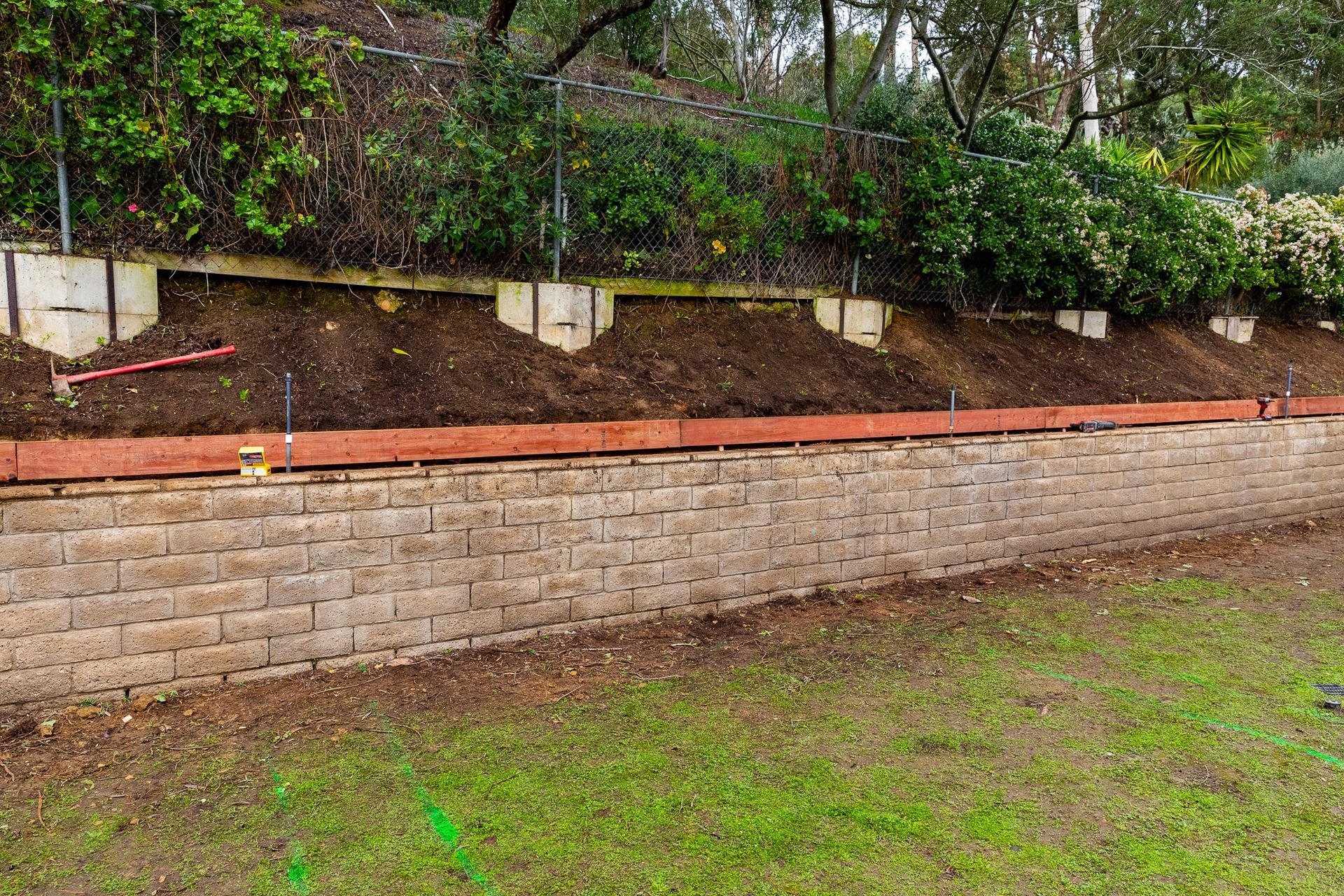 Retaining wall made of brick-like blocks, with soil behind it and grass in front.