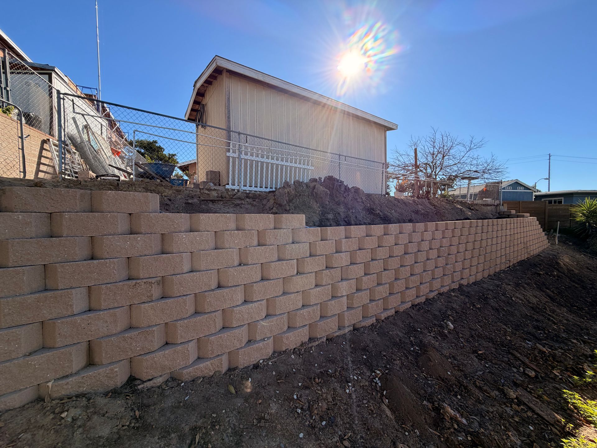 Stone-clad building with a balcony, lush green lawn, a leaning tree, and palm trees under a blue sky.