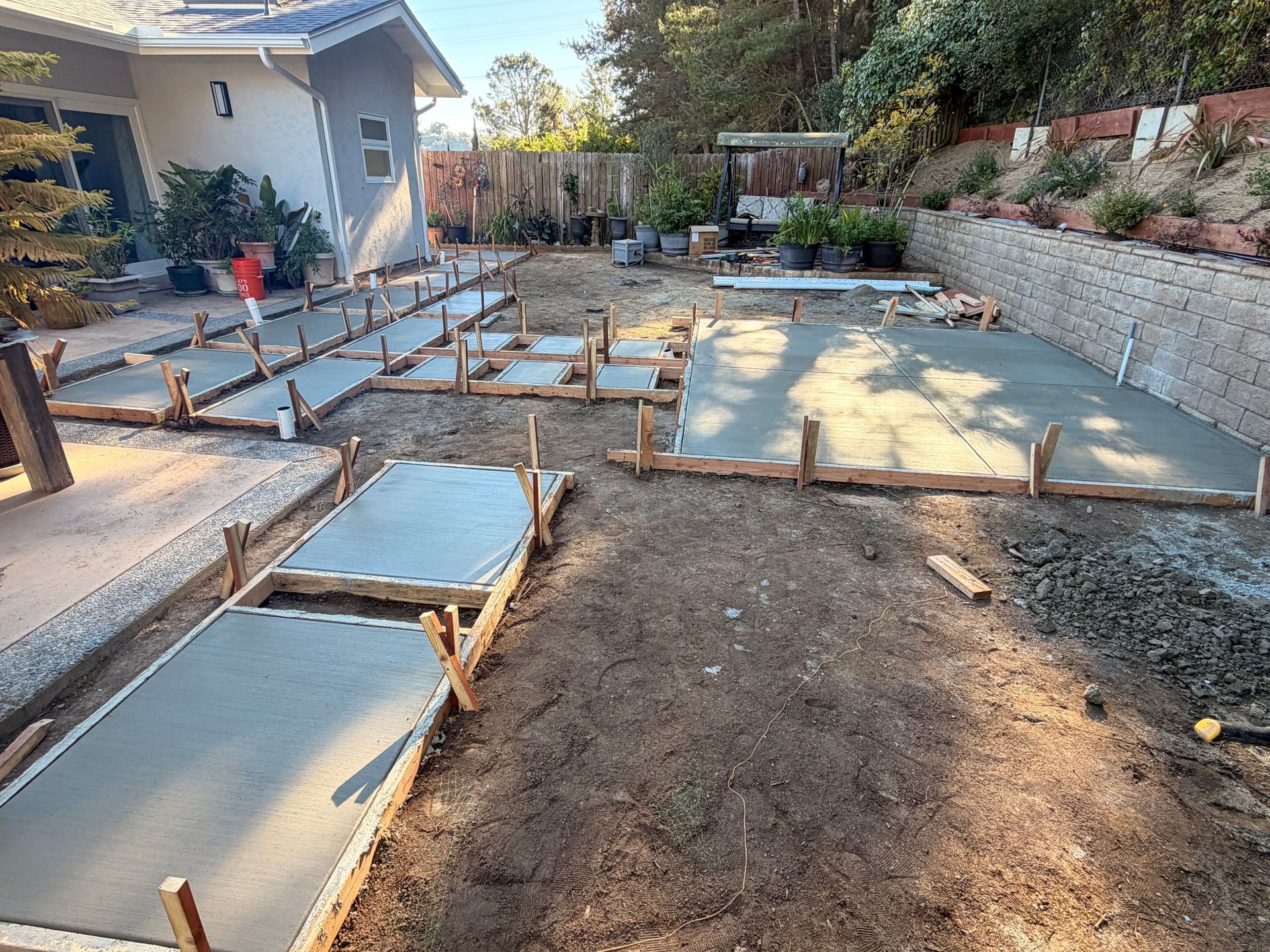 Two workers in caps and long sleeves outdoors: one points, other holds paperwork near a building.