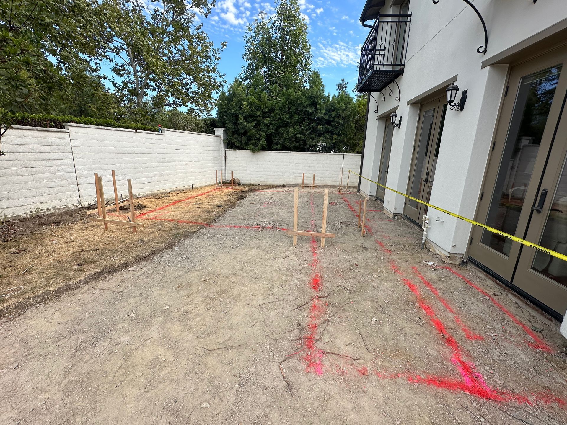 Gravel patio area marked with red spray paint and stakes, next to a white building. Construction site.