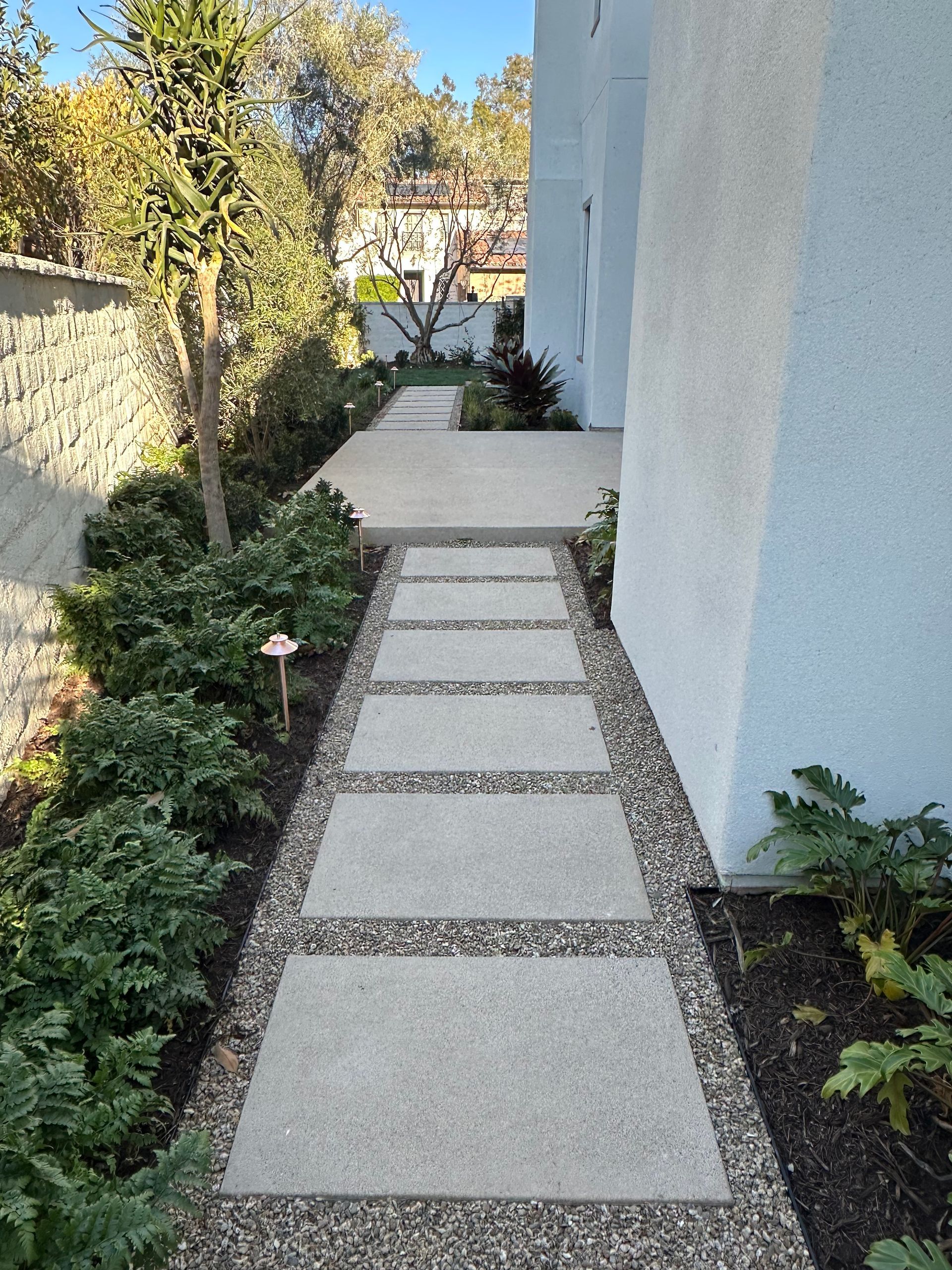 Concrete pathway with gravel borders and shrubbery leading to a building's entrance.