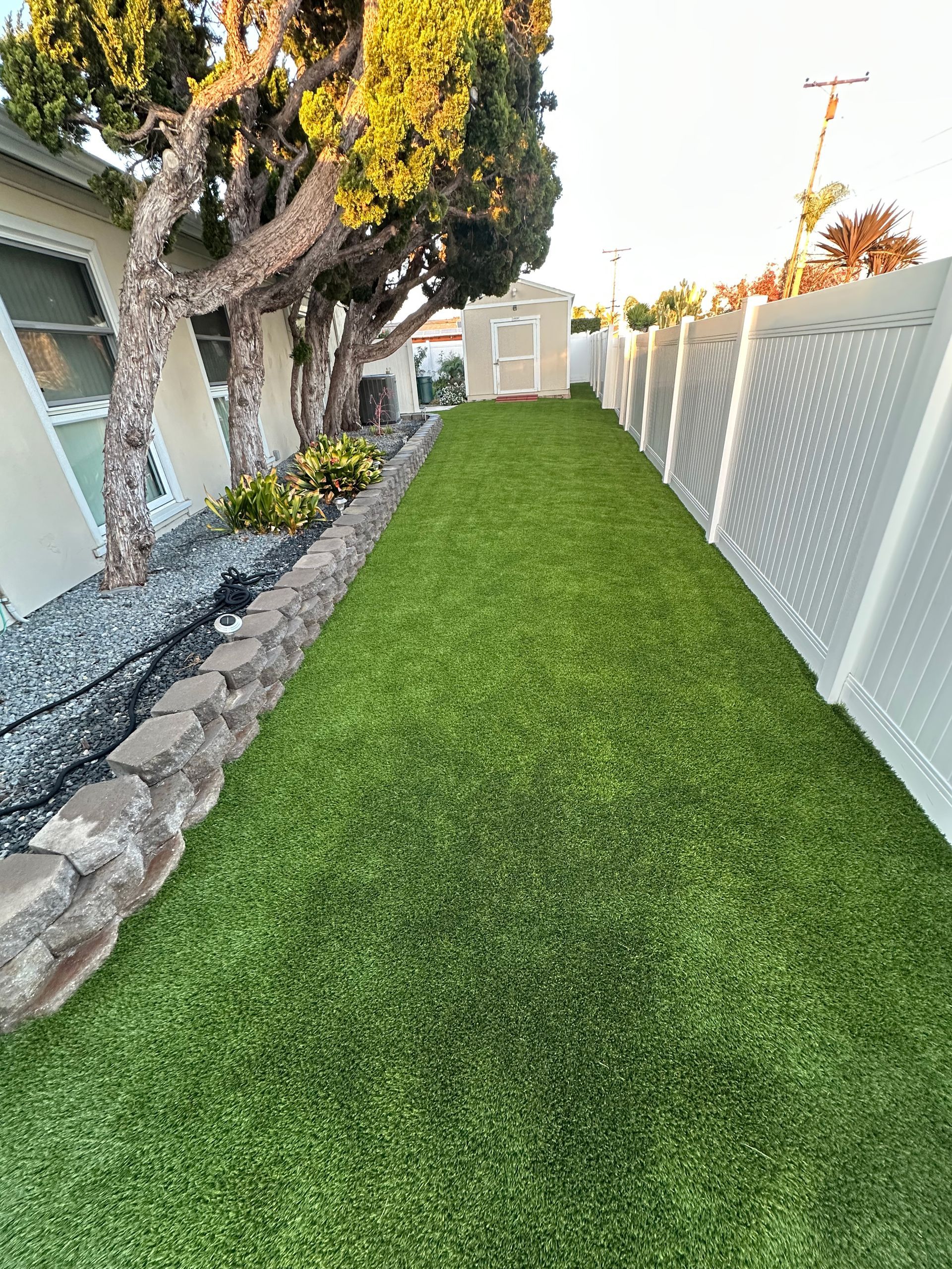 Stone-clad building with a balcony, lush green lawn, a leaning tree, and palm trees under a blue sky.
