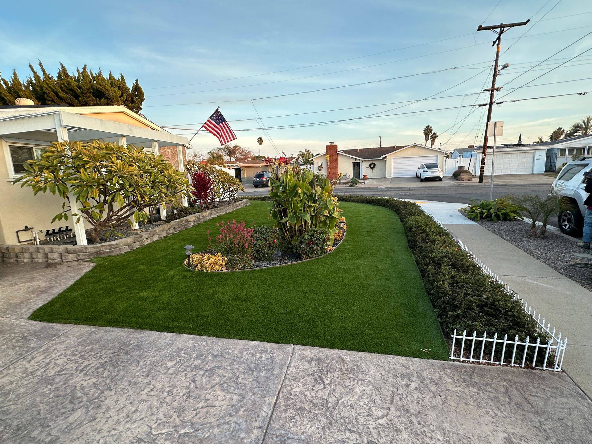 A suburban house with green lawn, flag, and plants. Gray concrete driveway. Overcast sky.