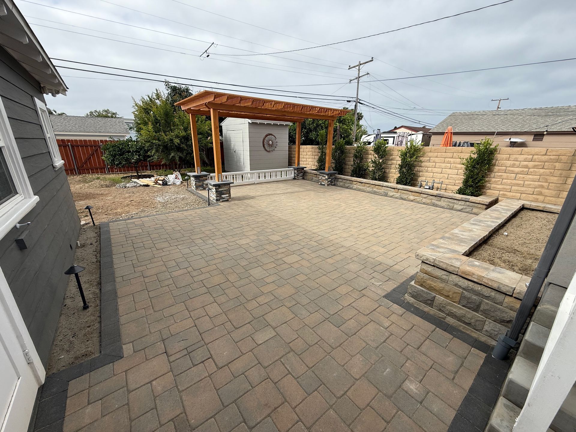 Backyard patio with brick pavers, a wooden pergola, and retaining walls.