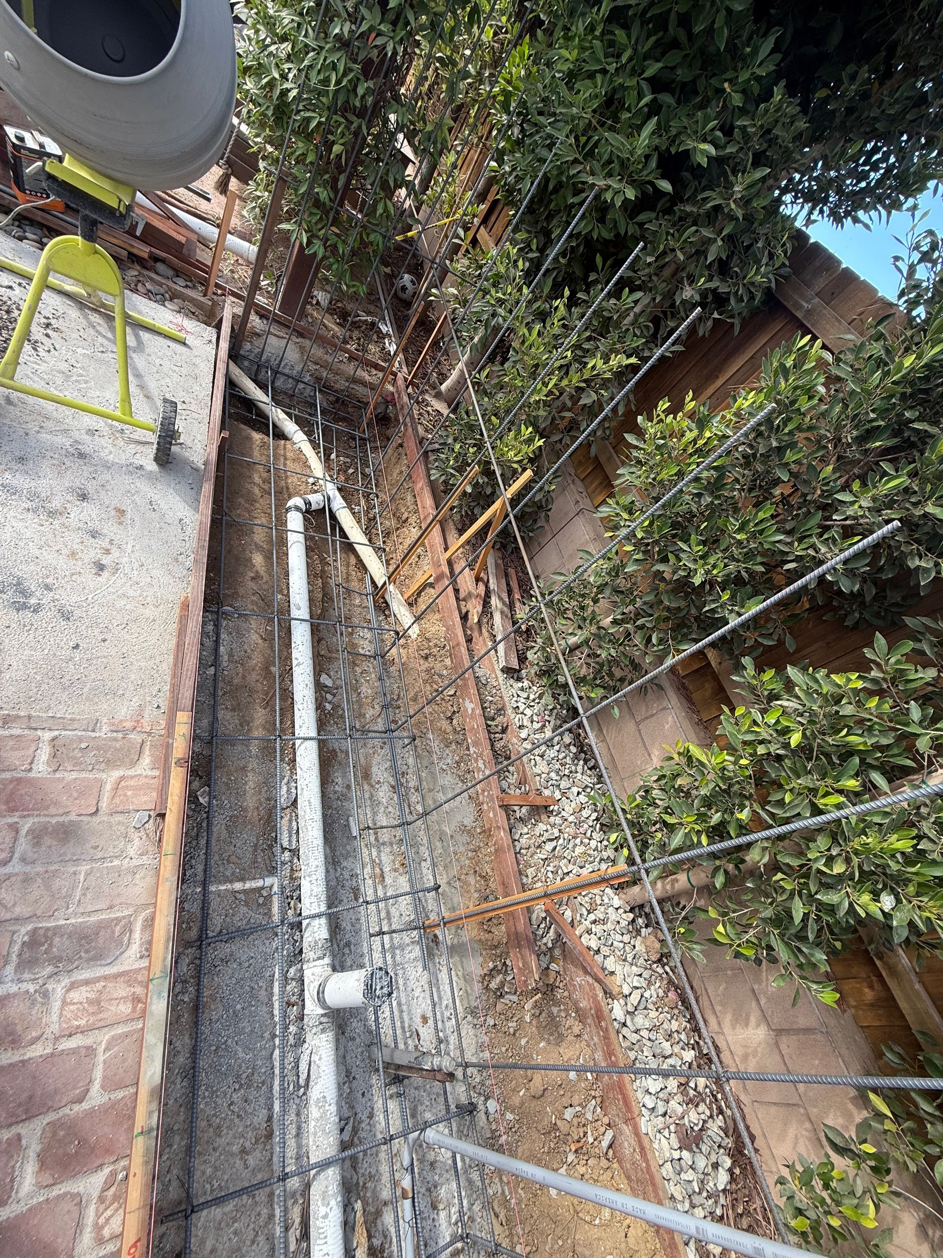 View of a narrow brick-walled alleyway with climbing plants, a drainpipe, and support wires.