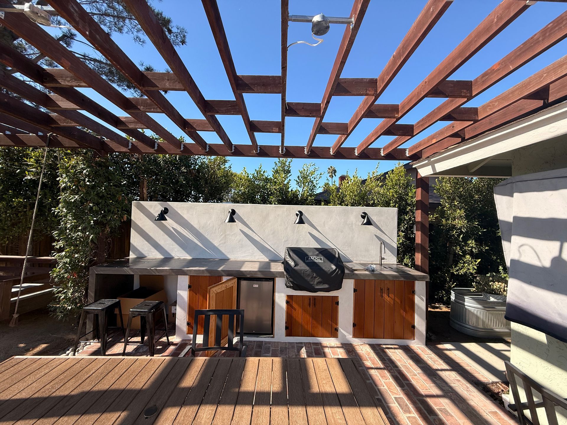 Outdoor kitchen with wooden pergola, concrete counter, grill, and cabinets.