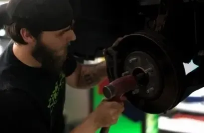 Zima mechanic working on a car wheel hub with a tool in a dim garage