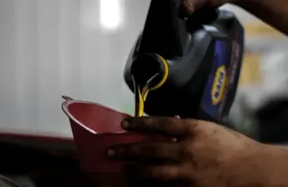 Zima mechanic pouring yellow liquid from a black bottle into a pink cup