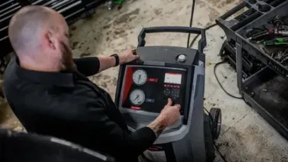 Zima mechanic operating a wheeled industrial machine with gauges and controls in a workshop.