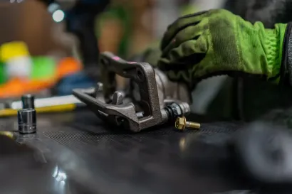 Mechanic using a tool to work on a car wheel hub, with a brake rotor visible in a garage.