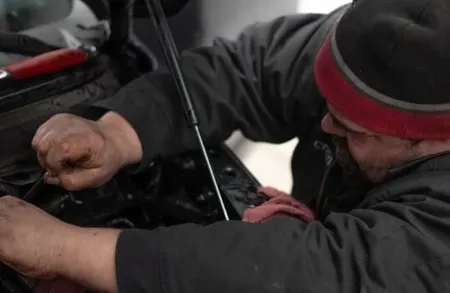 Man in dark jacket and red beanie working on a motorcycle engine, with hands greasy from repair