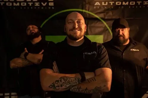 Three Zima team members pose with crossed arms in front of a dark automotive backdrop.