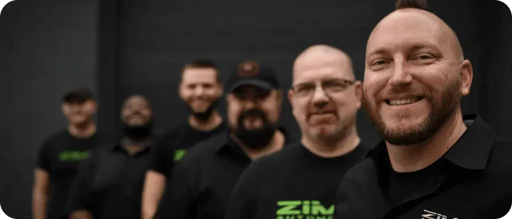 Smiling Zima team in black shirts posing together indoors, with one man in the foreground.