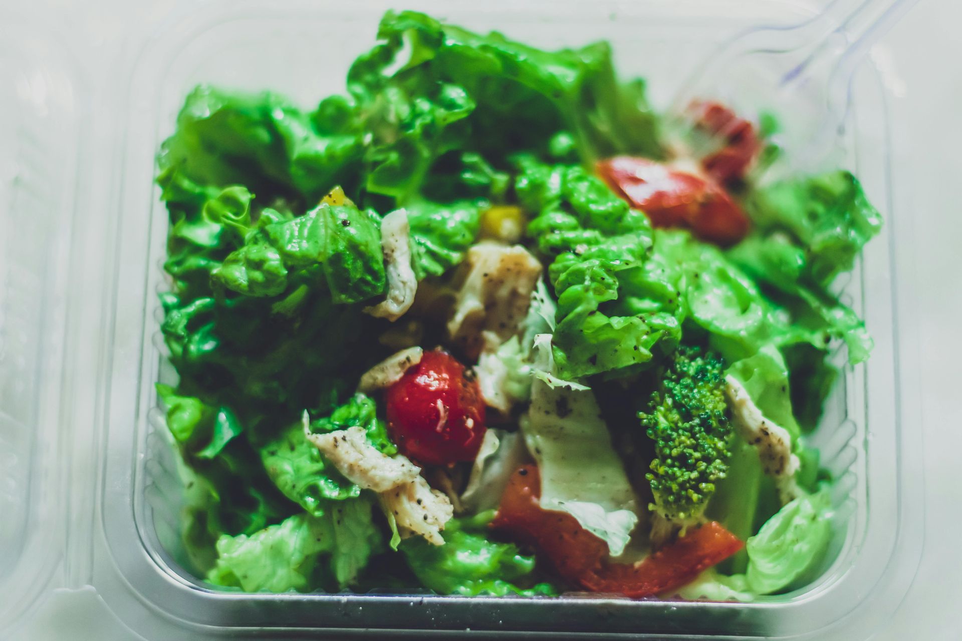 A close up of a salad in a plastic container with a fork.