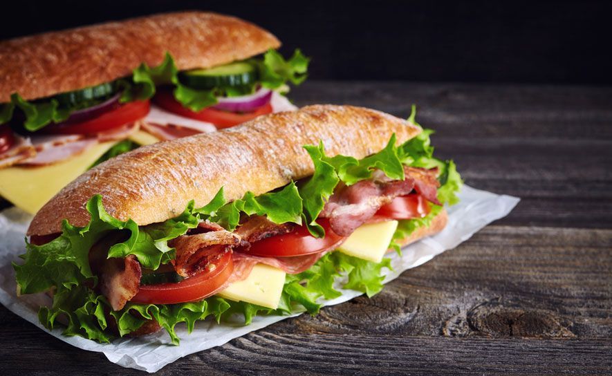 Two sub sandwiches are sitting on a wooden table.