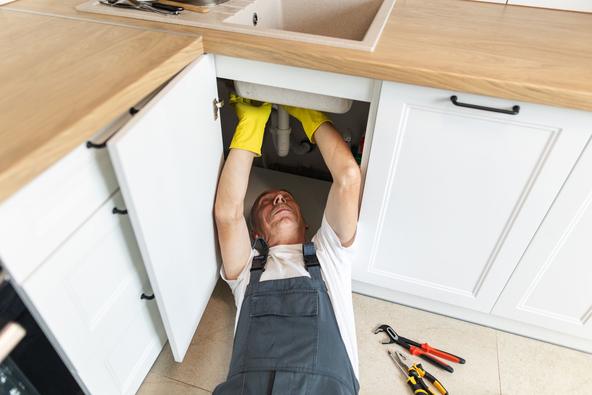 A man wearing gloves is fixing a faucet.