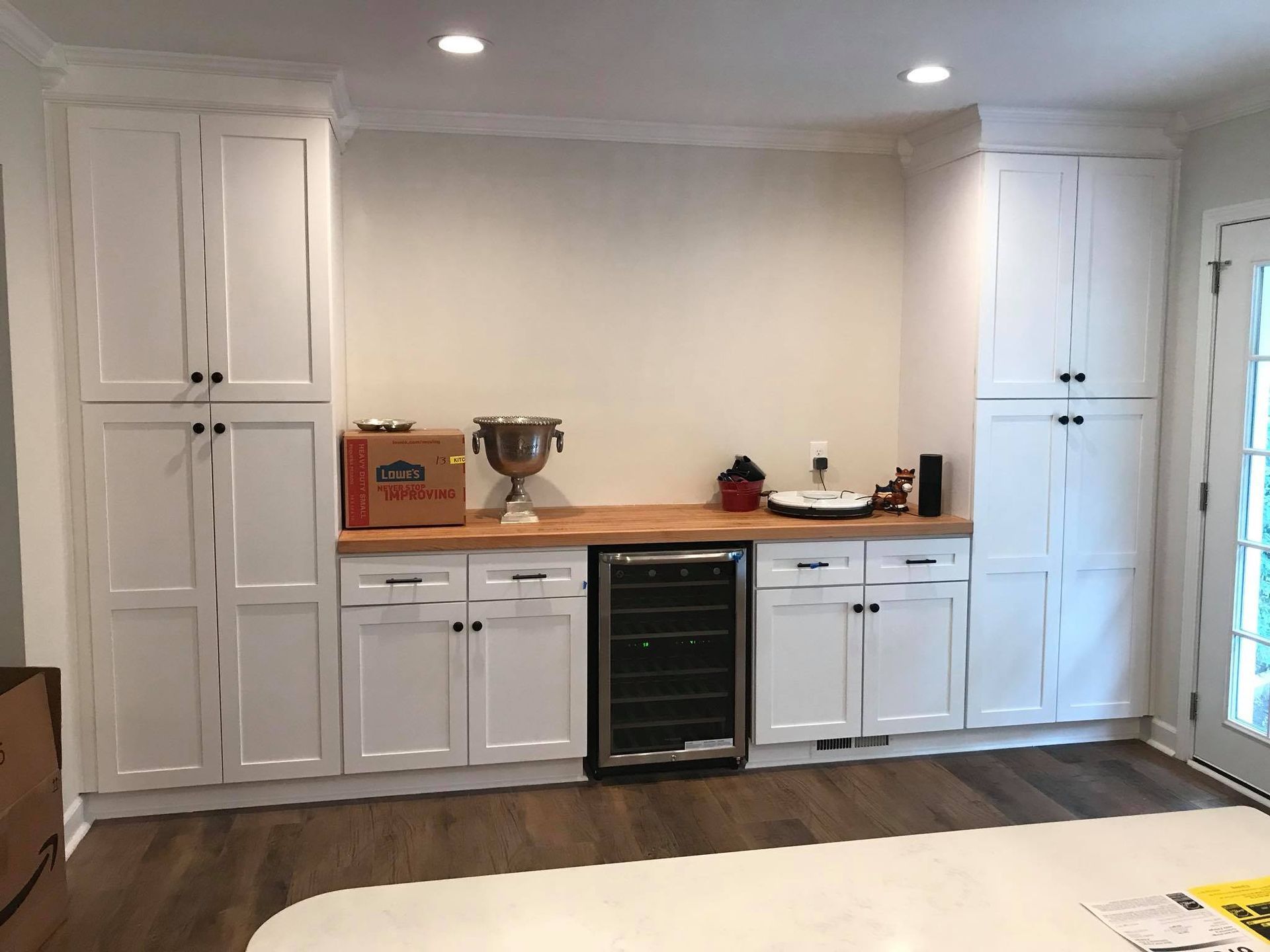 White kitchen cabinets with a wine fridge, butcher block countertop, and upper storage.