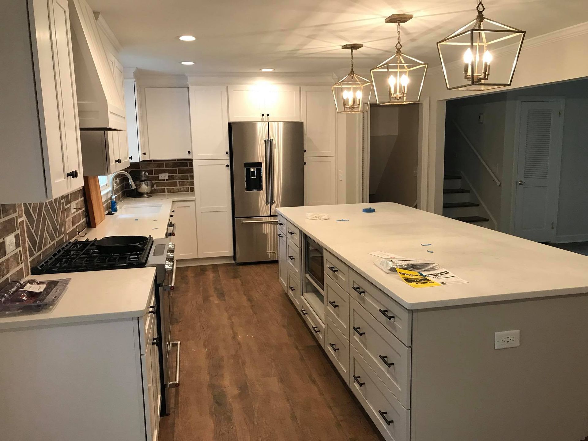 Newly remodeled white kitchen with island, stainless steel appliances, and hardwood floors.