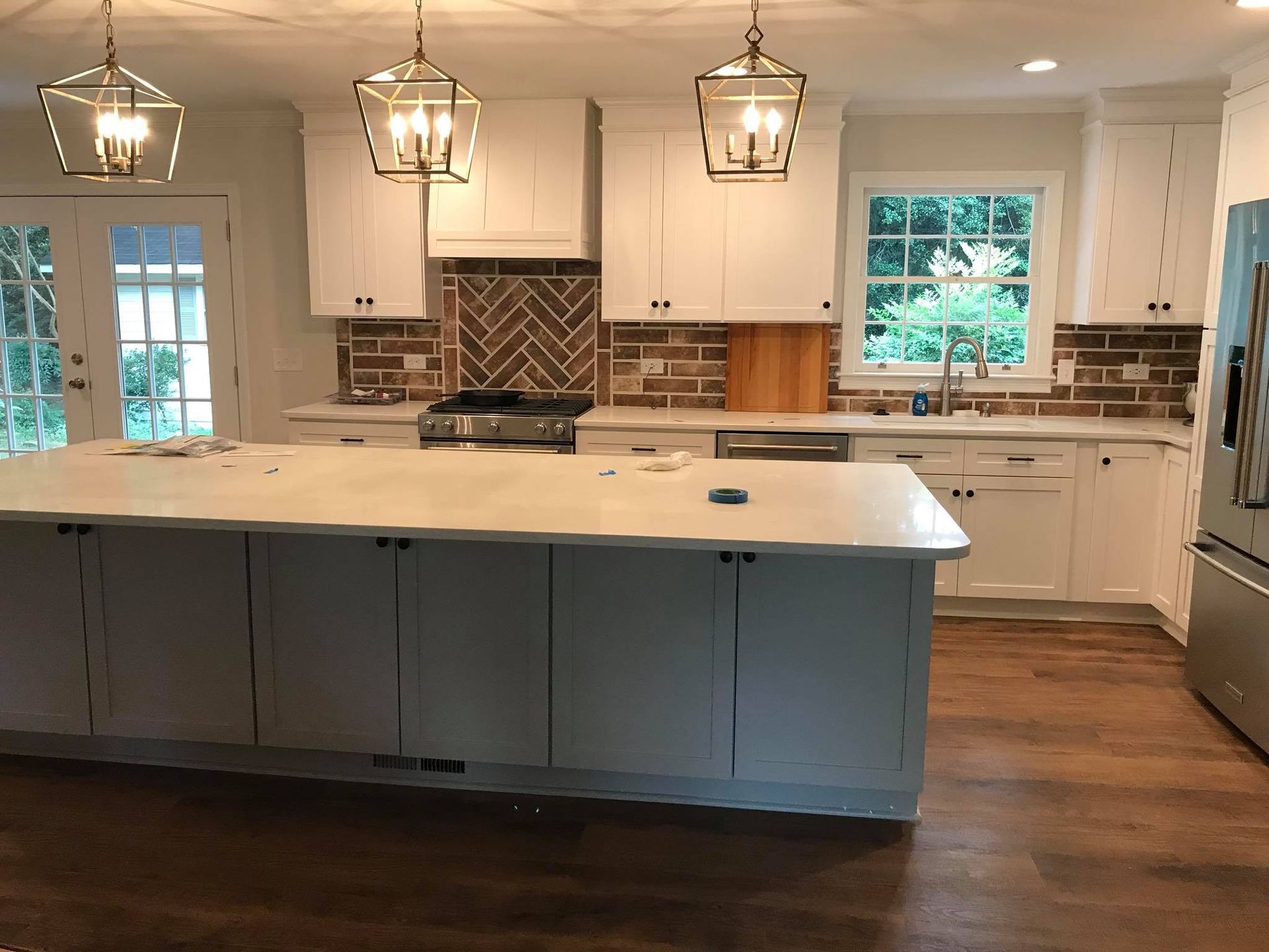 Modern kitchen with white cabinets, gray island, and brick backsplash.