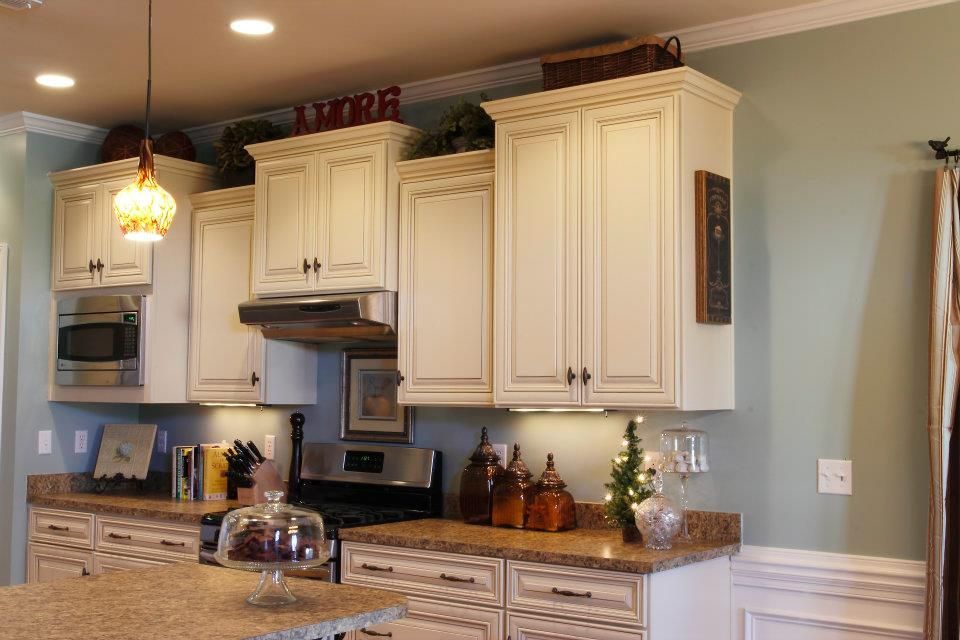 Cream-colored kitchen cabinets with countertops, and appliances. Teal walls with molding.