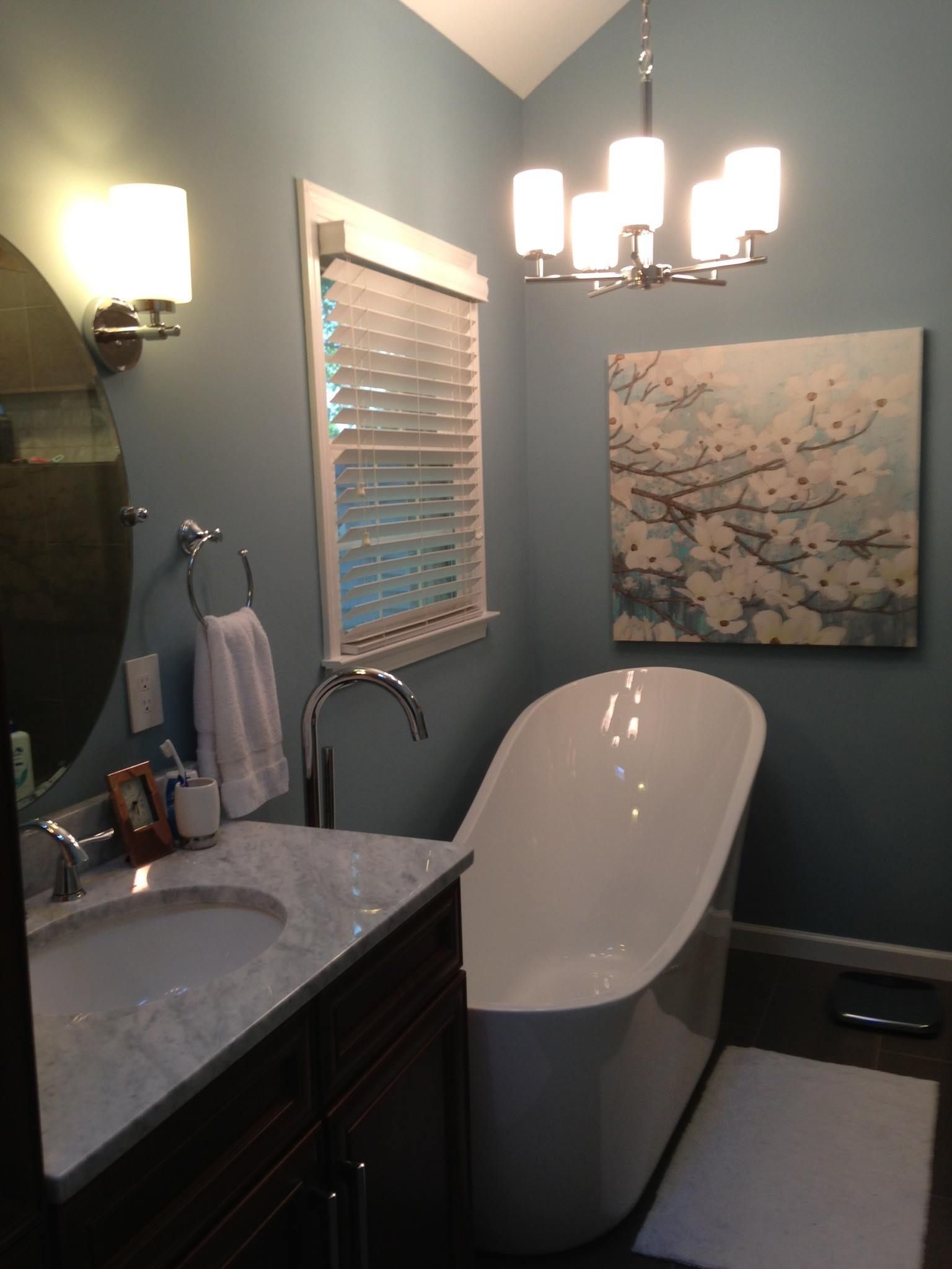 Bathroom with a white freestanding tub, sink, and artwork on a blue wall.
