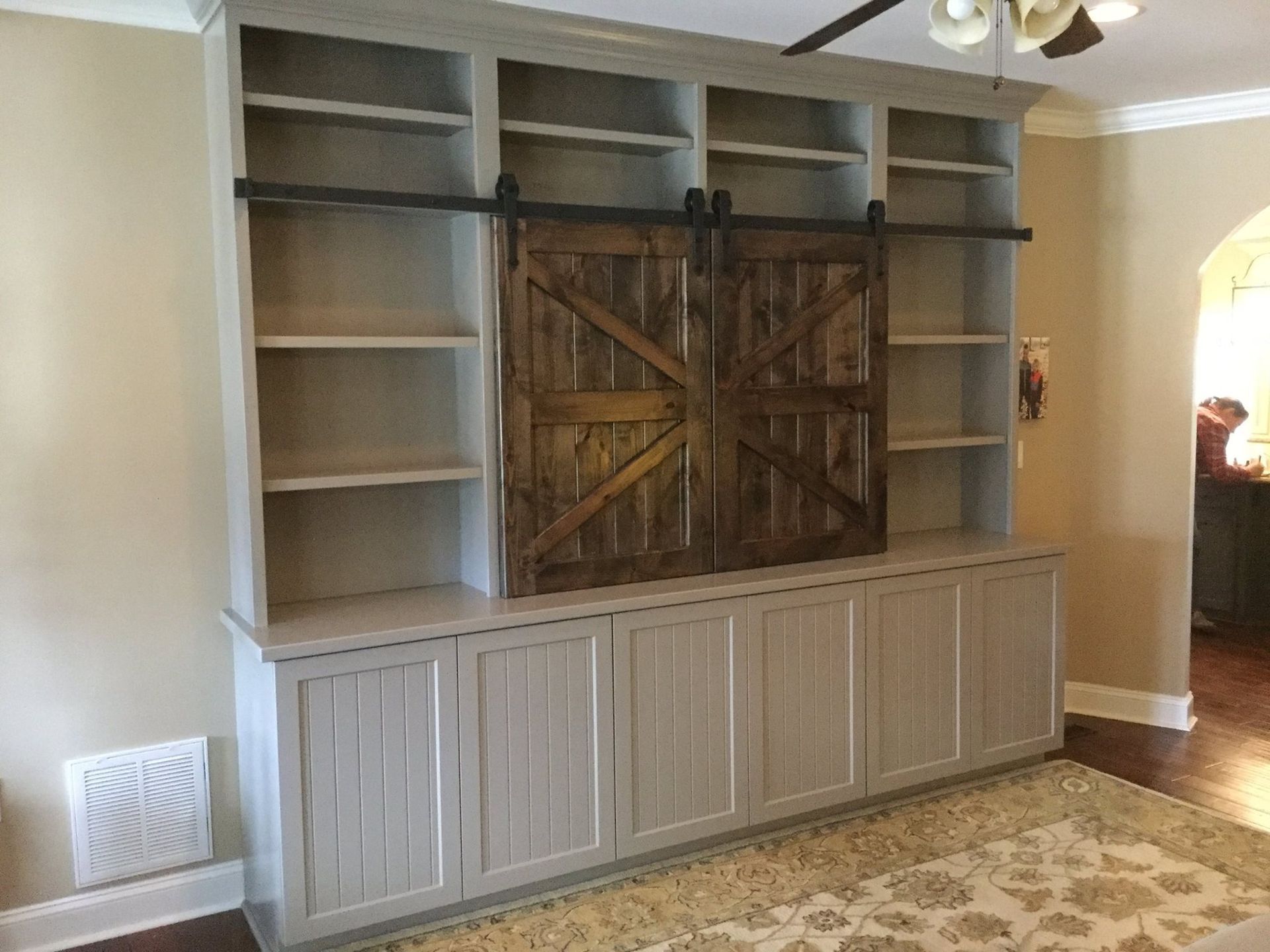 Built-in gray bookcase with sliding barn doors. Interior shelving and lower cabinets.