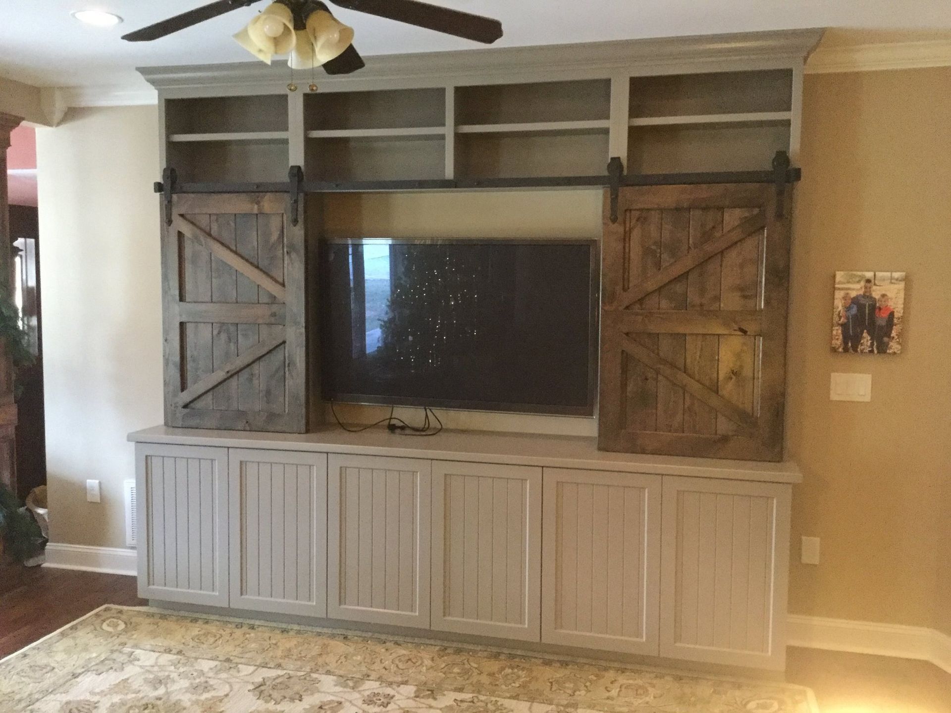 Built-in entertainment center with gray and wood accents, sliding barn doors, and a mounted TV.