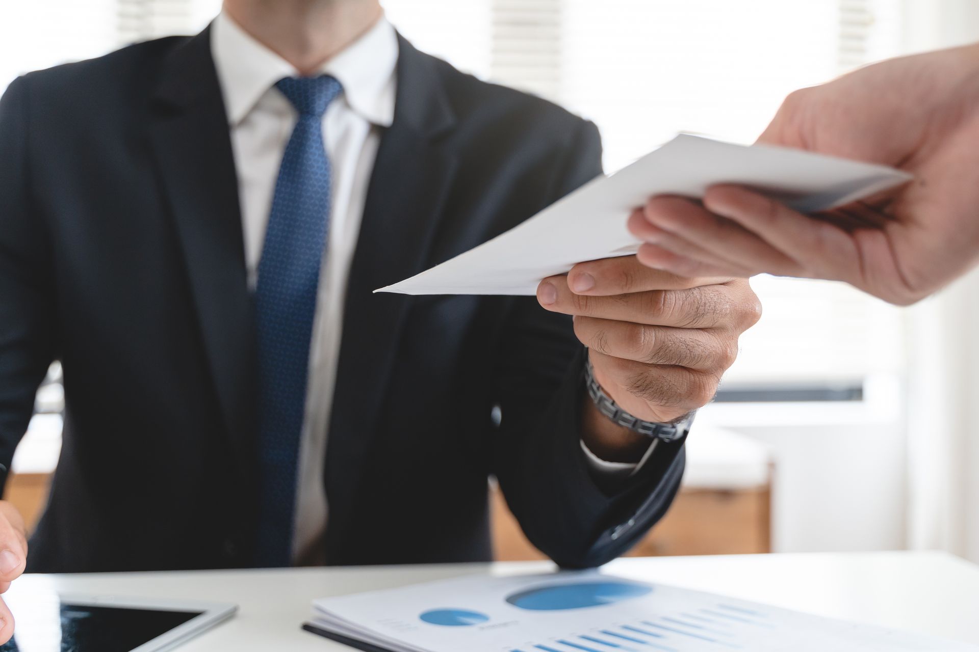 A man in a suit and tie is handing a piece of paper to another man.