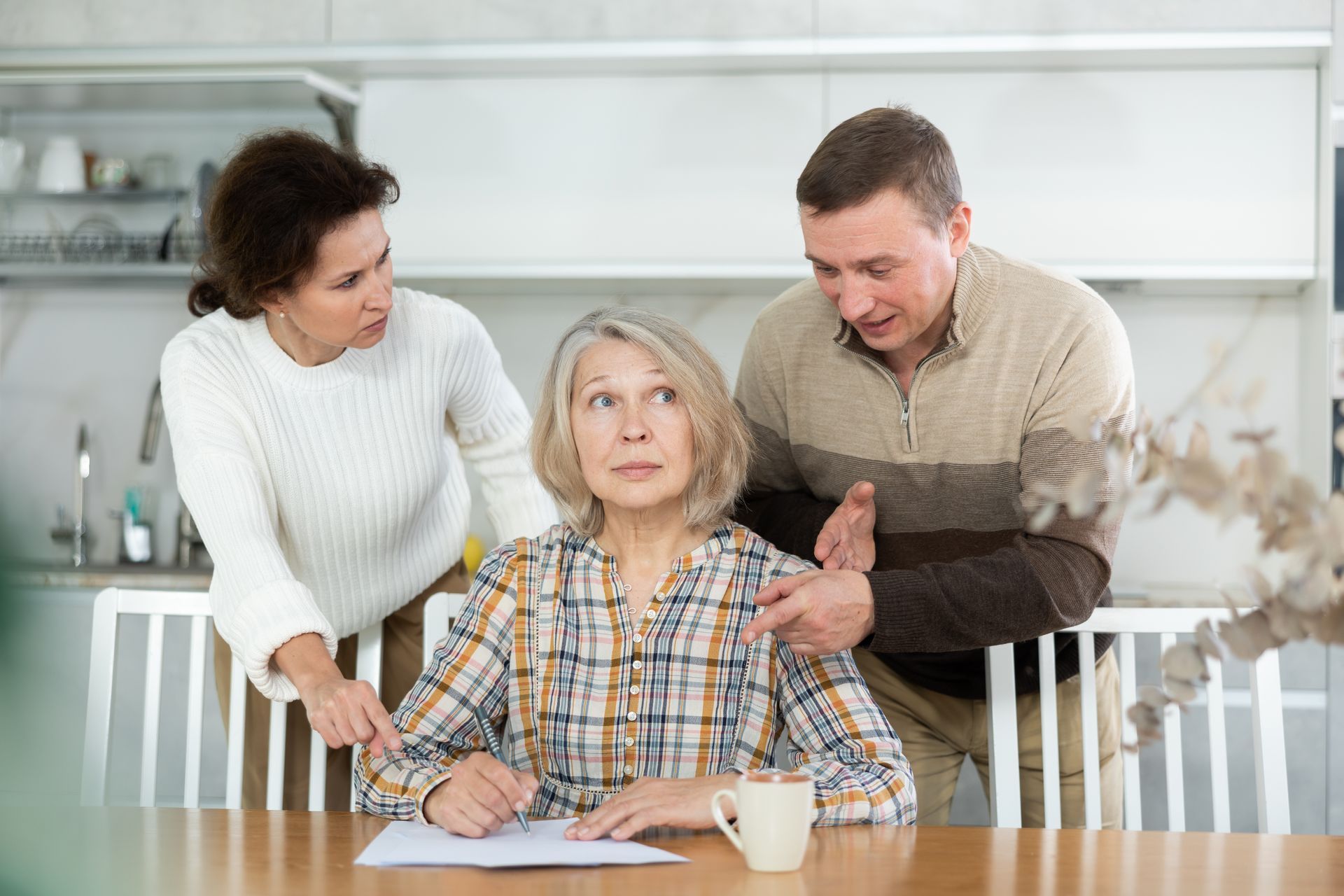 A man and two women are standing around a woman sitting at a table.