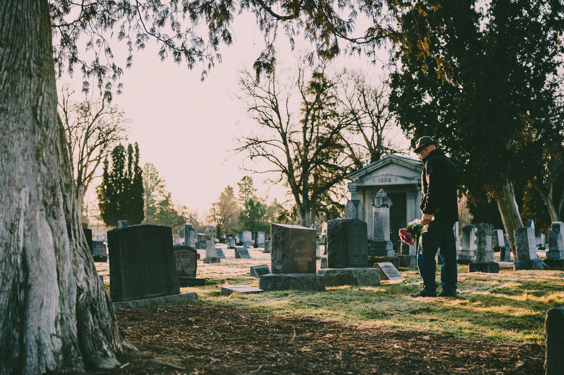 Ein Mann steht auf einem Friedhof und hält eine Blume in der Hand.