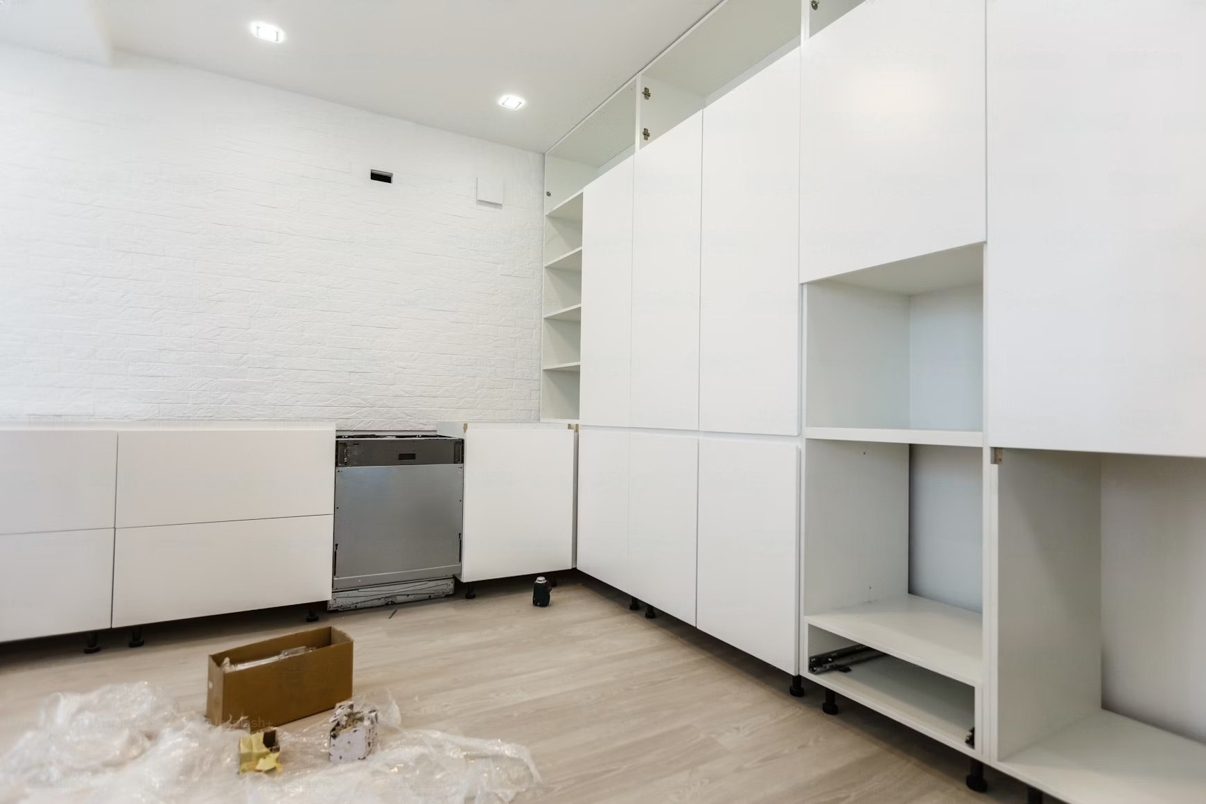 White kitchen cabinets and shelving in a room with light wood floors and exposed brick wall.
