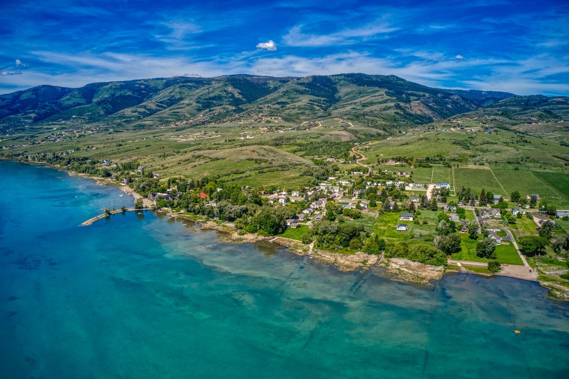 An aerial view of a small town on the shore of a lake with mountains in the background.
