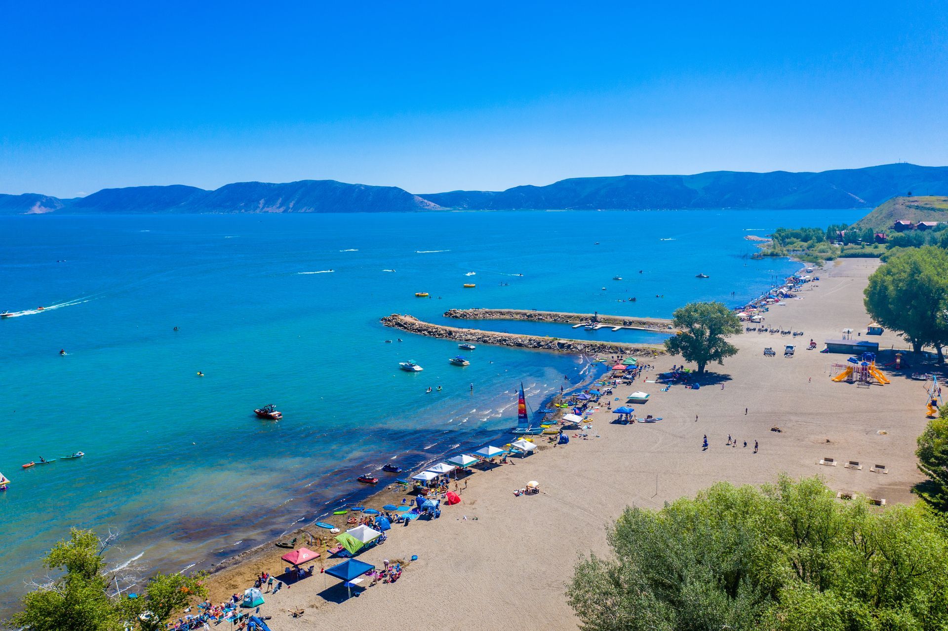 An aerial view of a beach filled with people and umbrellas next to a body of water.