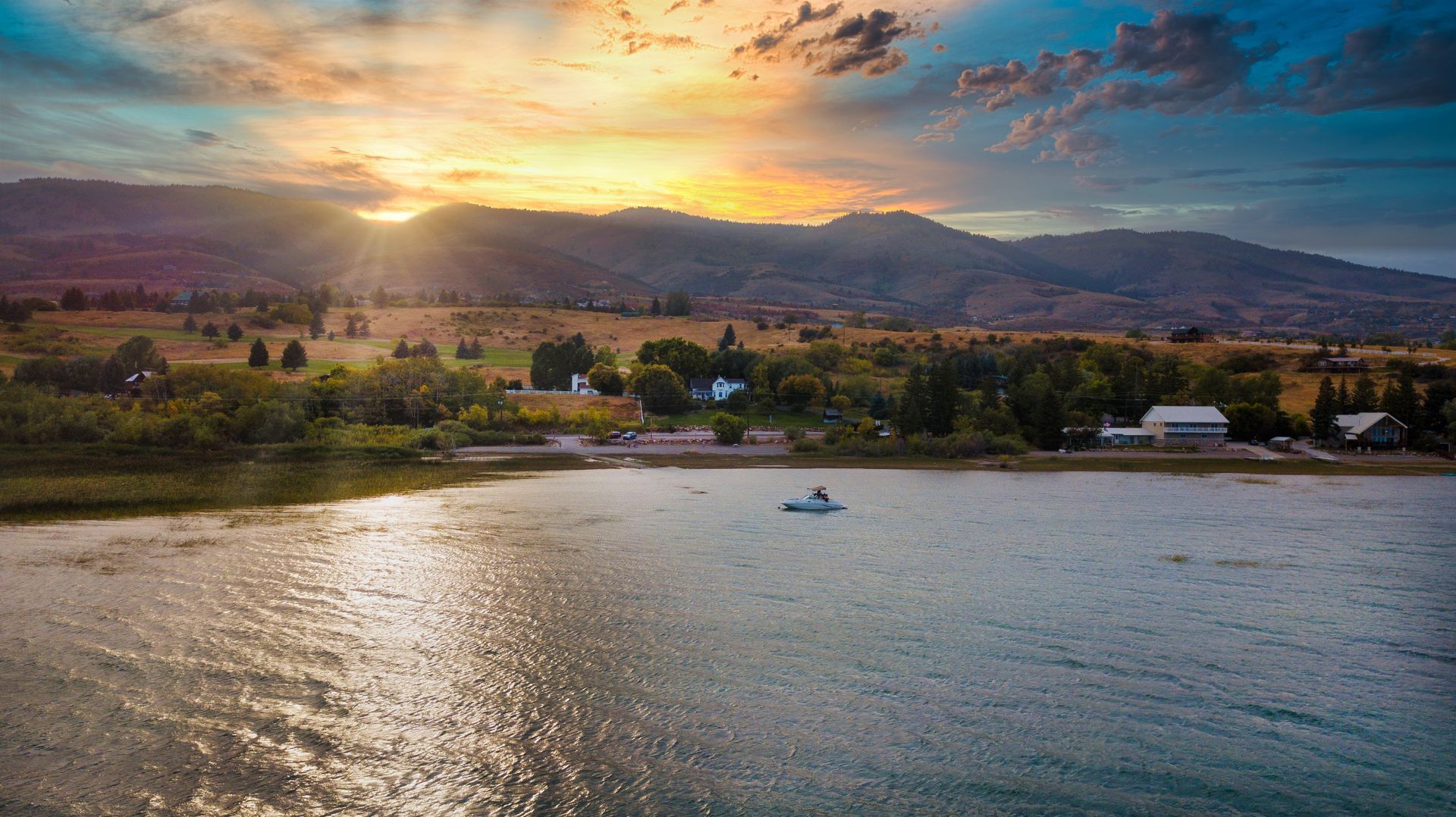 A boat is floating on a lake at sunset with mountains in the background.