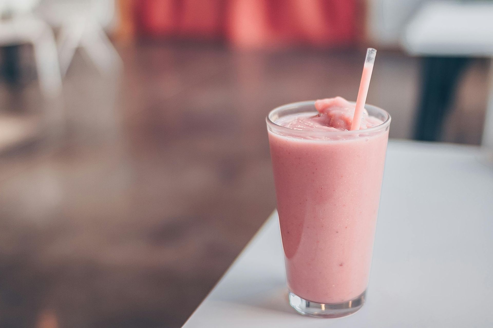 A close up of a pink milkshake with a straw on a table.