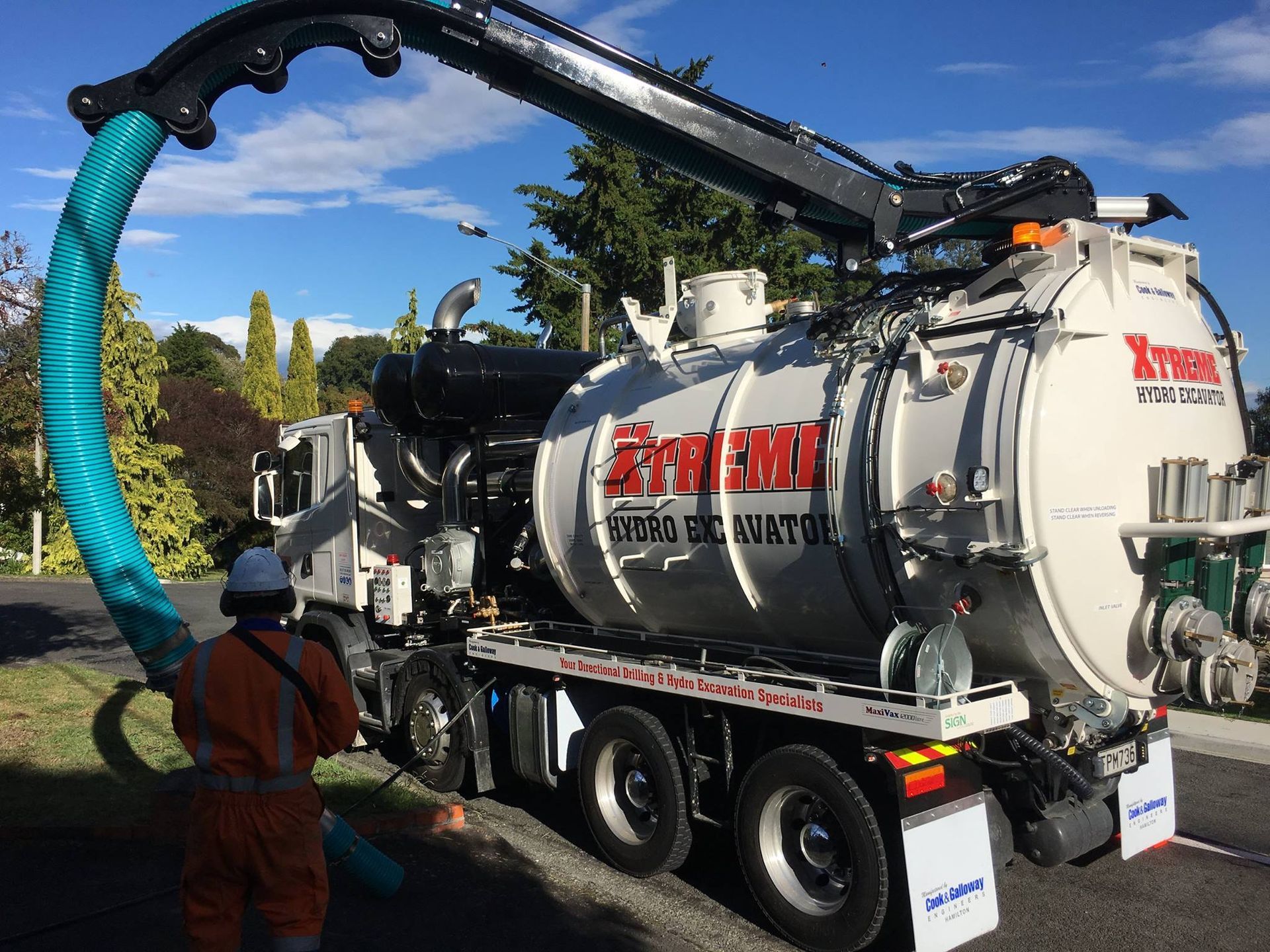 A man is standing next to a vacuum truck with a blue hose attached to it.