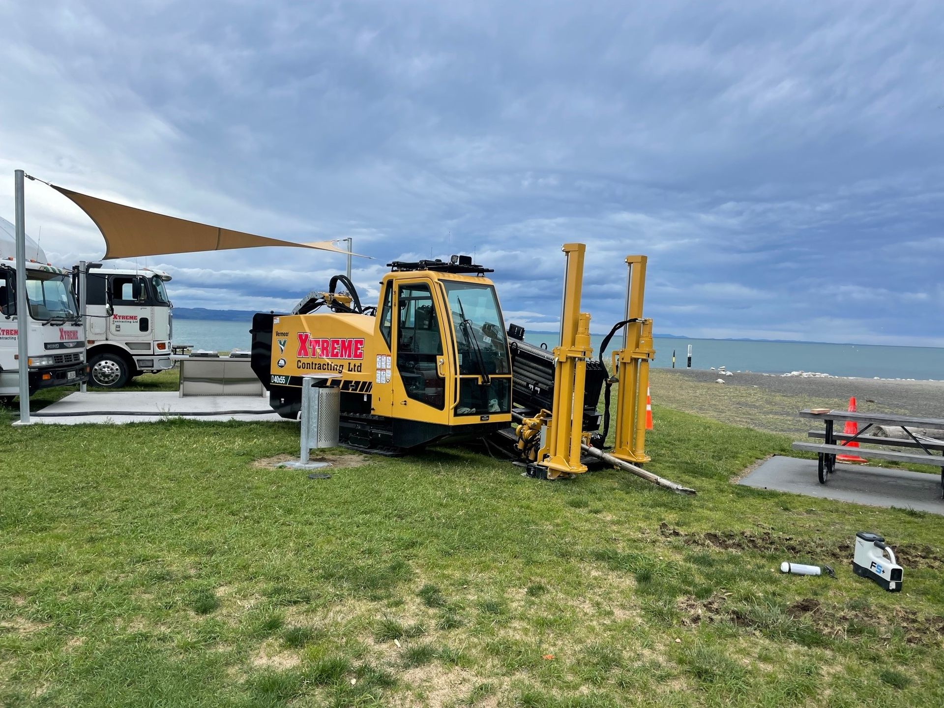 A yellow tractor is parked in a grassy field next to a beach.