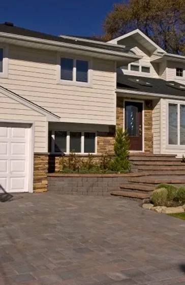 Two-story house with tan siding, stone accents, and a paved driveway.