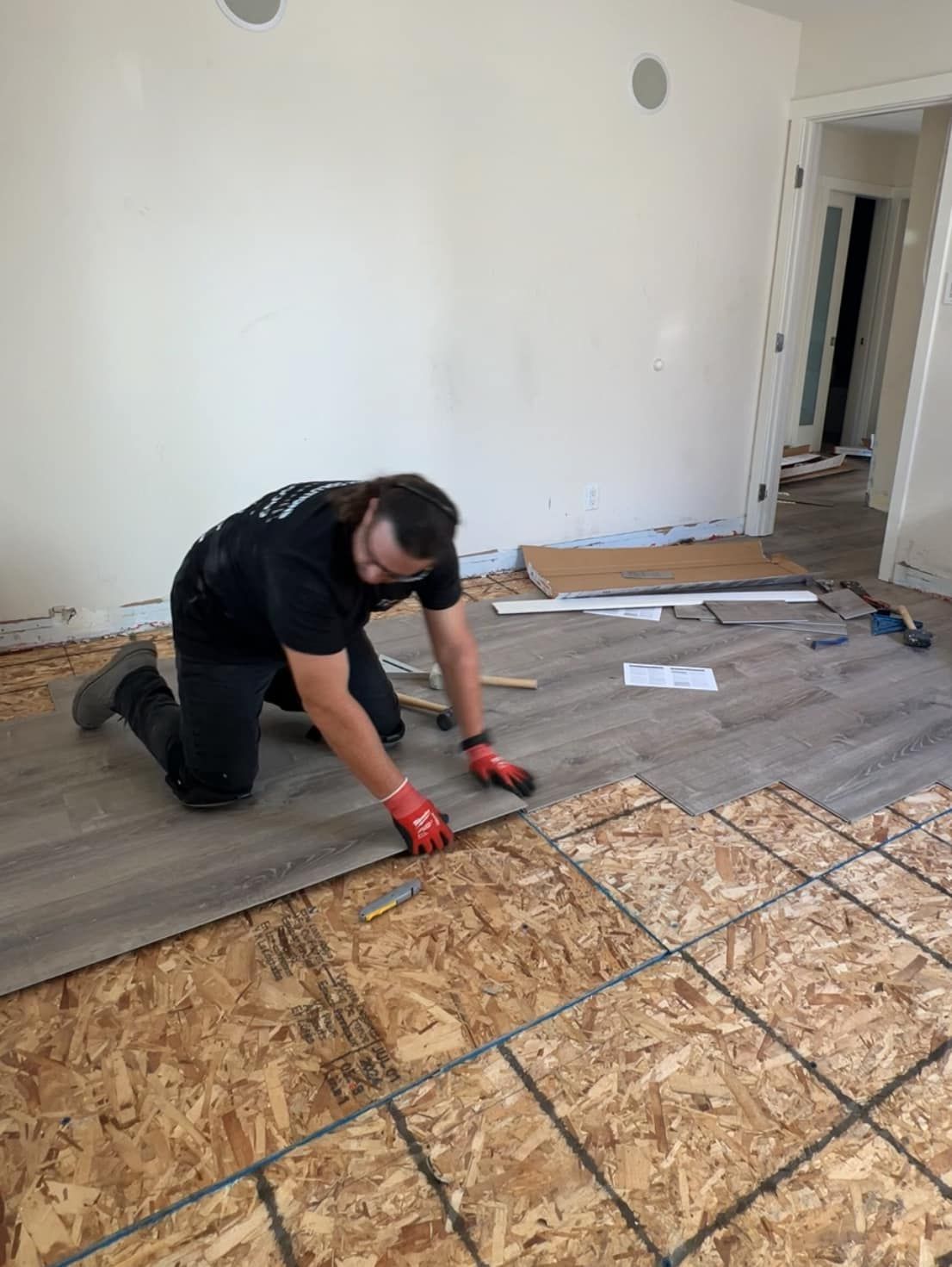 A man is kneeling on the floor while installing a wooden floor.